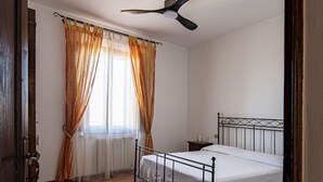 A bedroom with a bed, a ceiling fan, a window with curtains, and a patterned rug.