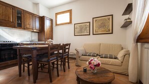 A cozy living room with a dining area, wooden cabinets, a sofa, and two framed maps on the wall.