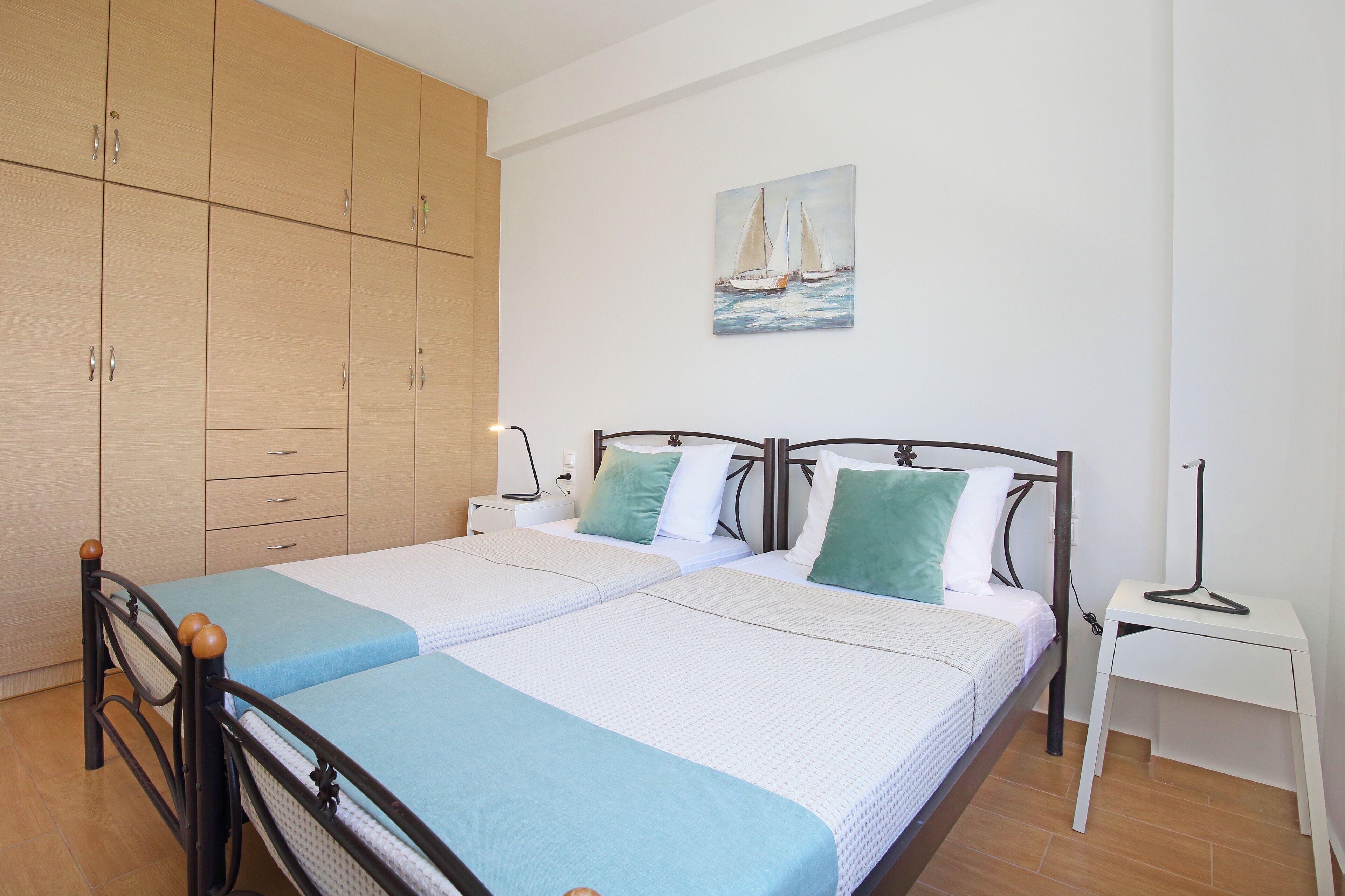 A double bed with a headboard, a nightstand, a white side table, and a wooden wardrobe.