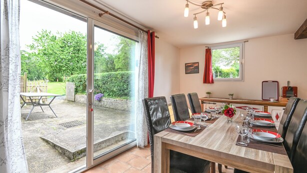 Comedor con mesa preparada para cuatro personas, puerta corredera de vidrio a un jardín y lámpara en el techo.