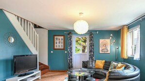 Una sala de estar con televisor, sofá, mesa de centro de vidrio, escalera y candelabro.
