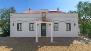 Um edifício branco com telhado de azulejos, entrada central com porta e duas janelas de cada lado.