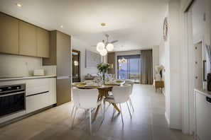 Una cocina moderna con electrodomésticos integrados, un comedor con mesa redonda y sillas blancas, y vistas al exterior.