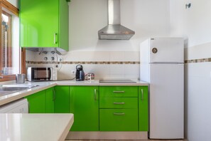 Uma cozinha com armários verdes, uma geladeira branca, micro-ondas e cafeteira.