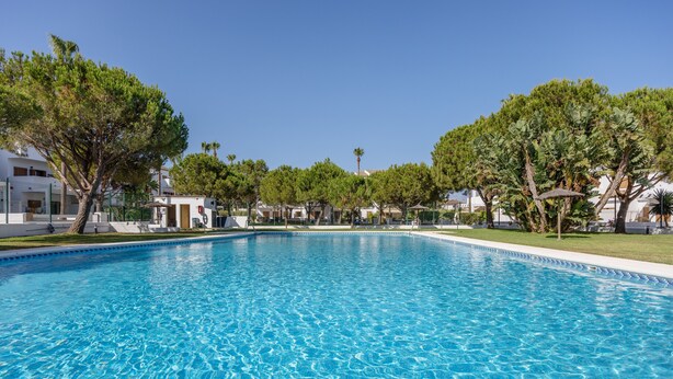 A clear swimming pool surrounded by trees and buildings.