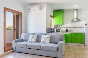 Uma sala de estar com um sofá cinza, uma cozinha verde com armários, um micro-ondas e uma geladeira.