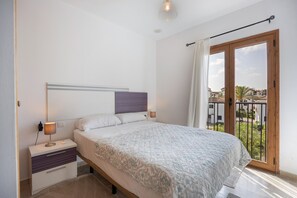A bedroom with a bed, bedside tables, a lamp, a window with curtains, and a view of buildings outside.