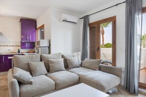 A modern living room with a beige sofa, a small kitchen area with purple cabinets, and a sliding glass door leading to an outdoor area. - Apartment 'Viento Del Mar' with Shared Pool, Private Terrace and Air Conditioning. (Chiclana de la Frontera)