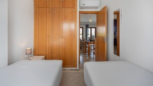 Une chambre avec deux lits, une armoire en bois, un bureau et un coin repas visible à travers une porte ouverte.