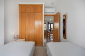 A bedroom with two beds, a wooden wardrobe, a desk, and a dining area visible through an open door. - Apartment 'Viento Del Mar' with Shared Pool, Private Terrace and Air Conditioning. (Chiclana de la Frontera)