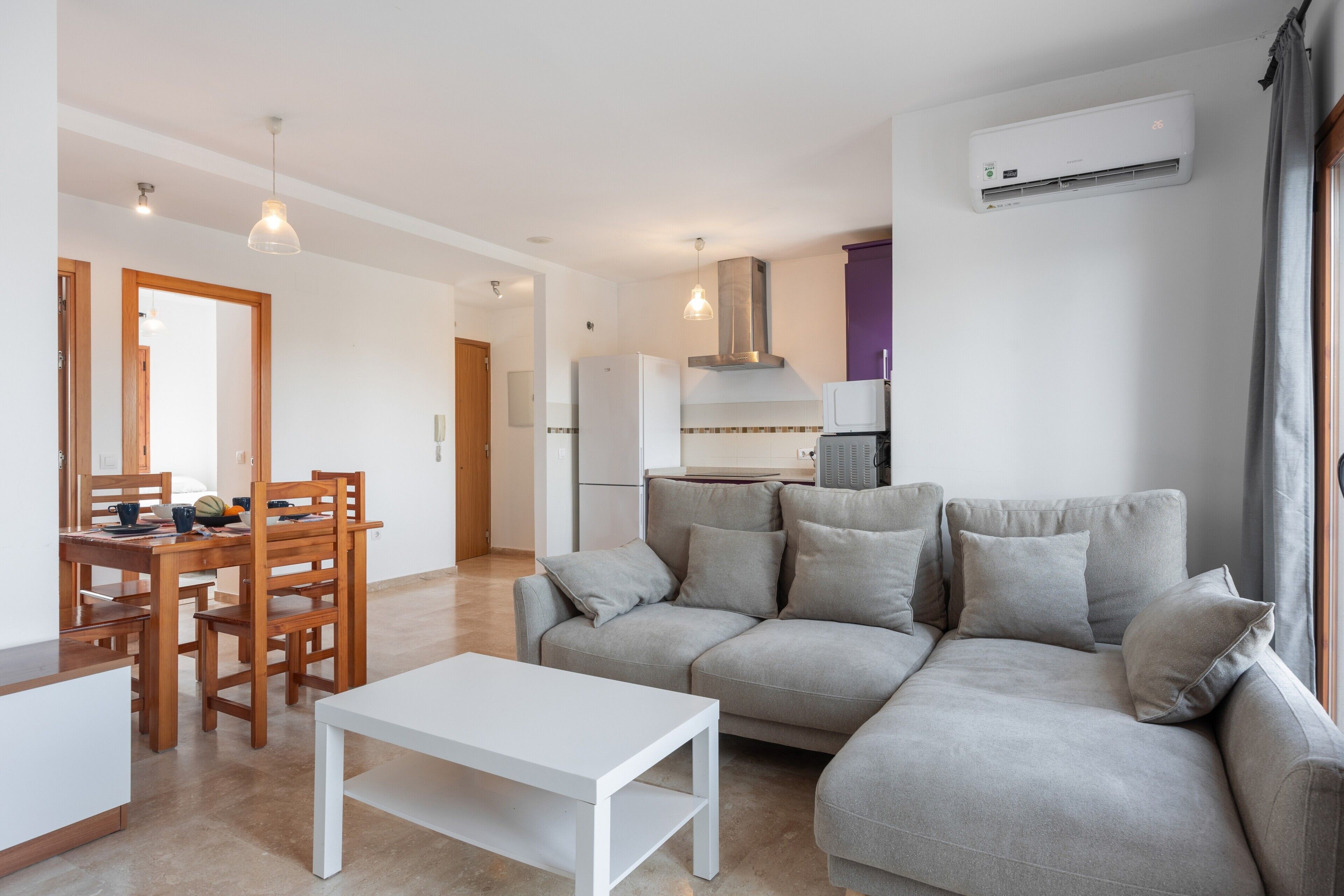 Una sala de estar moderna con un sofá, una mesa de comedor con sillas y una cocina al fondo.
