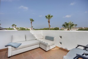 A white sectional sofa with a blue throw pillow on a tiled patio.