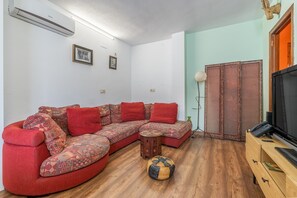 A living room with a sectional sofa, a small wooden side table, a patterned ottoman, a television, and a decorative wall panel. - Apartment 'Granada David' with Shared Terrace, Wi-Fi and Air Conditioning (Granada)