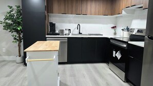 A modern kitchen with black and white cabinetry, a wooden countertop, and stainless steel appliances. - 🏡 Spacious Basement Suite: 2 queen beds, Kitchen, Livingroom, Dining, Laundry (Edmonton)