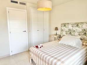 A bedroom with a bed, a nightstand, a lamp, a wall with a leaf pattern, and two white doors.