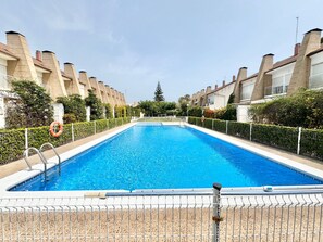 A rectangular swimming pool with a metal fence, surrounded by a row of buildings with similar architecture.