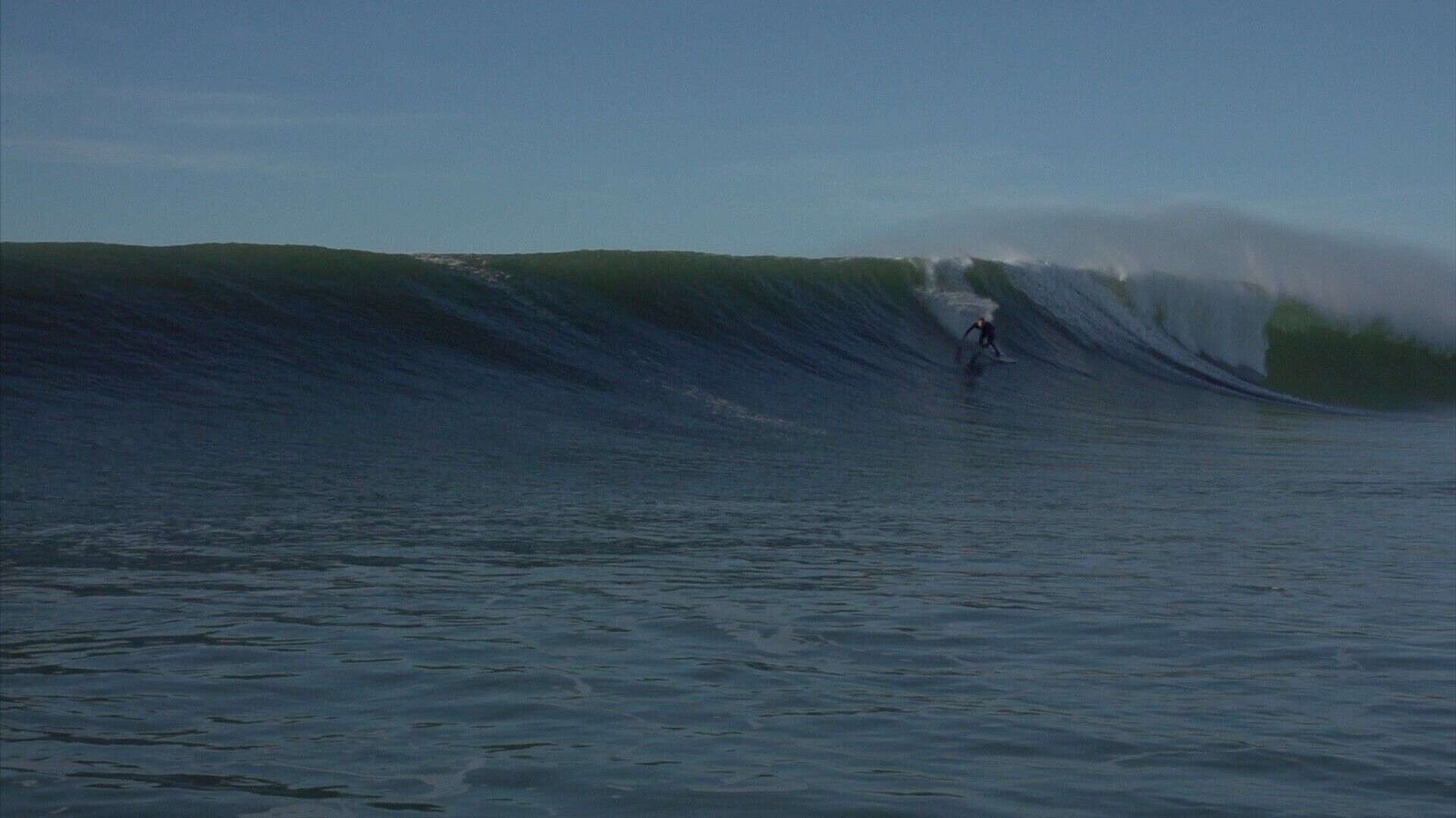 A large wave in the ocean with a surfer riding it.
