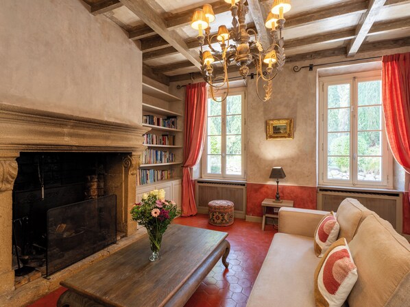 Una habitación acogedora con chimenea, estanterías, un sofá y una araña.