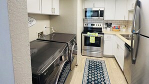 Uma cozinha compacta com armários brancos, micro-ondas, forno, máquina de lavar loiça e frigorífico.