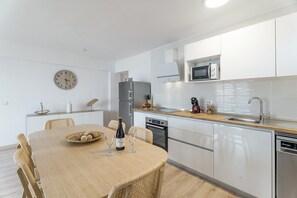 Een moderne keuken met witte kastjes, een magnetron, een koelkast en een eettafel met stoelen.