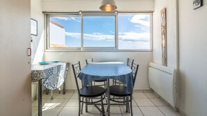 A dining area with a table and chairs, a window with a view, and a pendant light. - Apartment 'Les Balcons De La Méditerranée' with Sea View and Balcony (Narbonne-Plage)