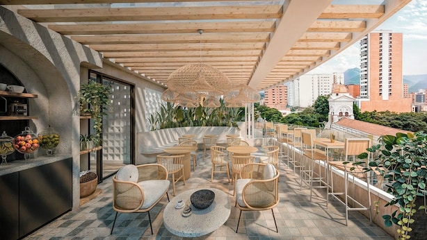 A rooftop terrace with wooden tables and chairs, a buffet area, and a view of the cityscape. - Hotel Tres Altares Sabaneta (Sabaneta)