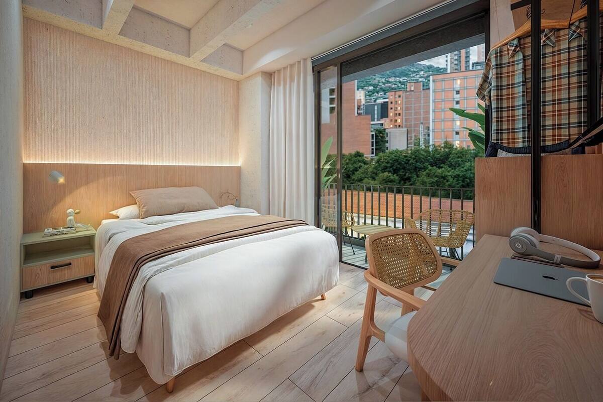 A modern bedroom with a bed, bedside table, chair, and a balcony with a view of buildings.