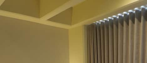 Habitación de hotel con una cama grande, cabecera con panel de luz, mesita de noche de madera y ventana con cortinas.