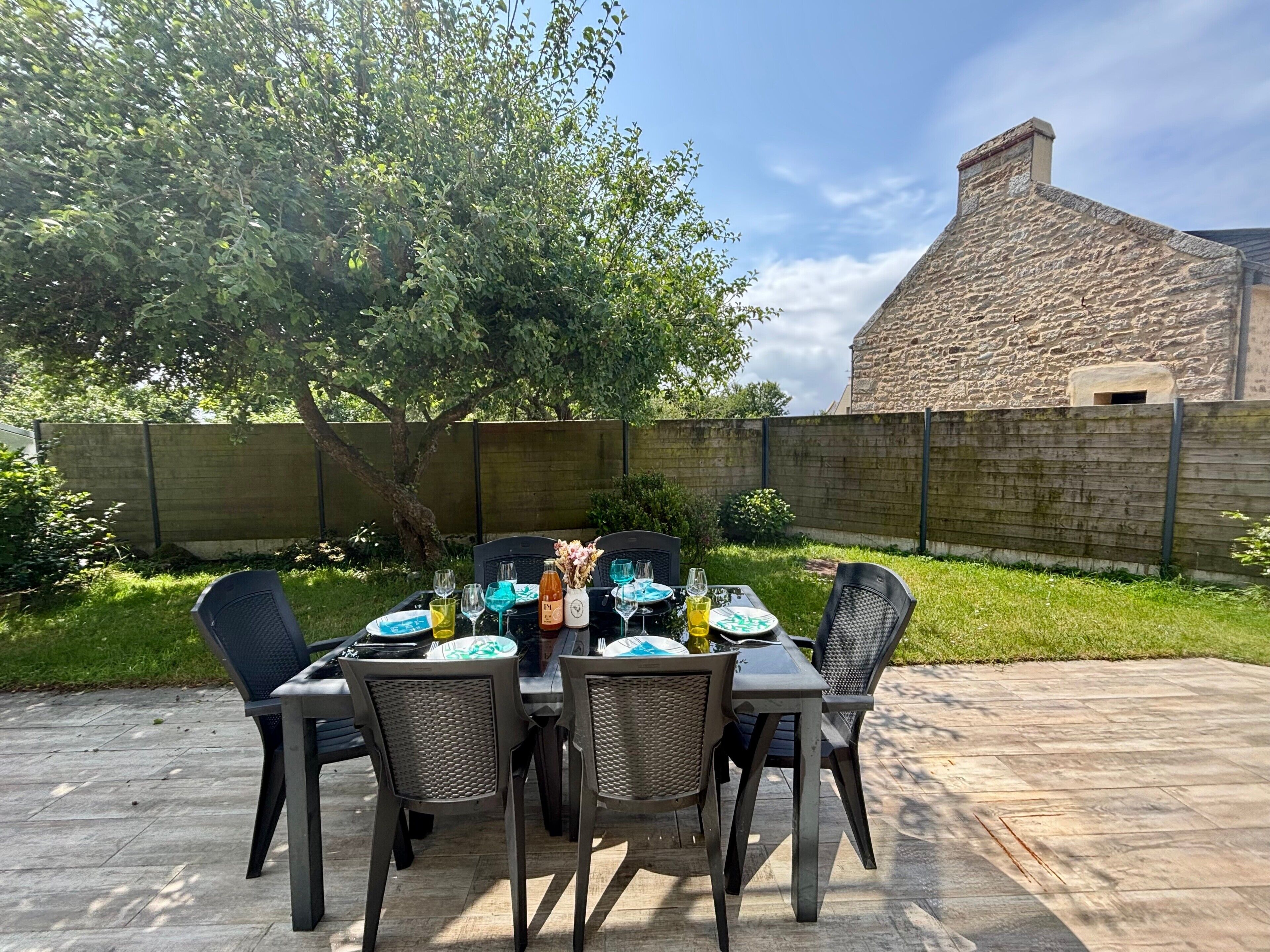 Une terrasse extérieure avec une table dressée pour quatre personnes, entourée de chaises, et un bâtiment en pierre en arrière-plan.