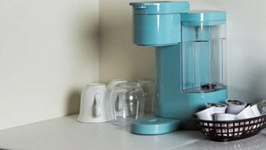 A coffee maker, several glasses, and a basket with cups on a countertop.