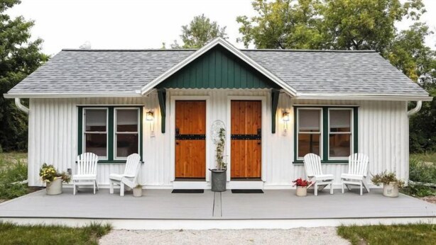 A small, single-story building with a gabled roof, two front doors, and a porch with white chairs.