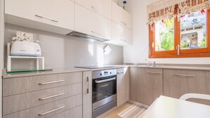 A modern kitchen with white cabinets, a built-in oven, and a window with lace curtains. - Holiday Home 'Son Amanada' with courtyard and Wi-Fi (Santa Margalida)