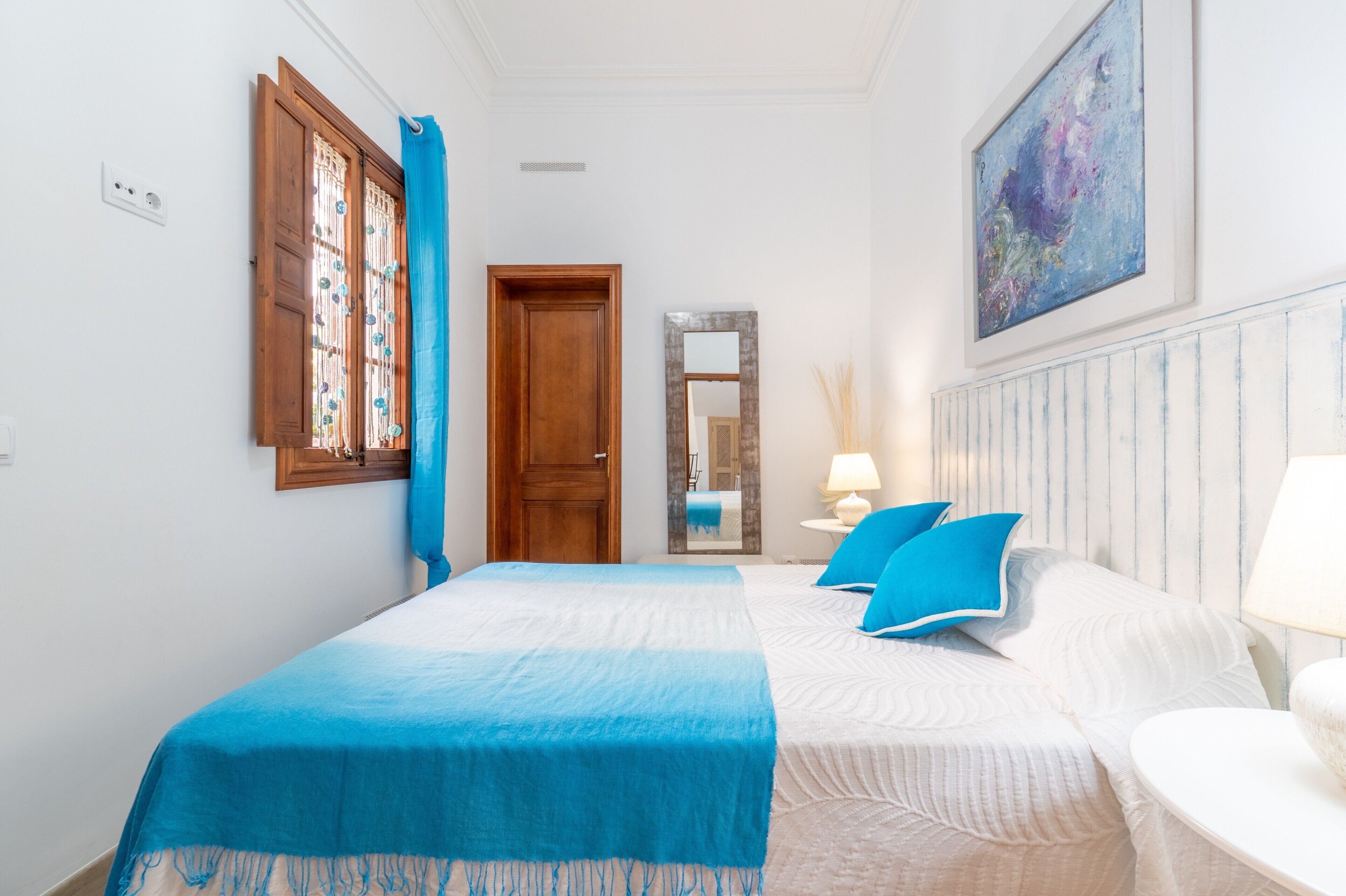 A bedroom with two beds, a wooden door, a mirror, and a painting on the wall.