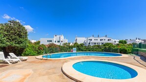 Un área de piscina con dos piscinas circulares, sillas de descanso y un cielo azul despejado.
