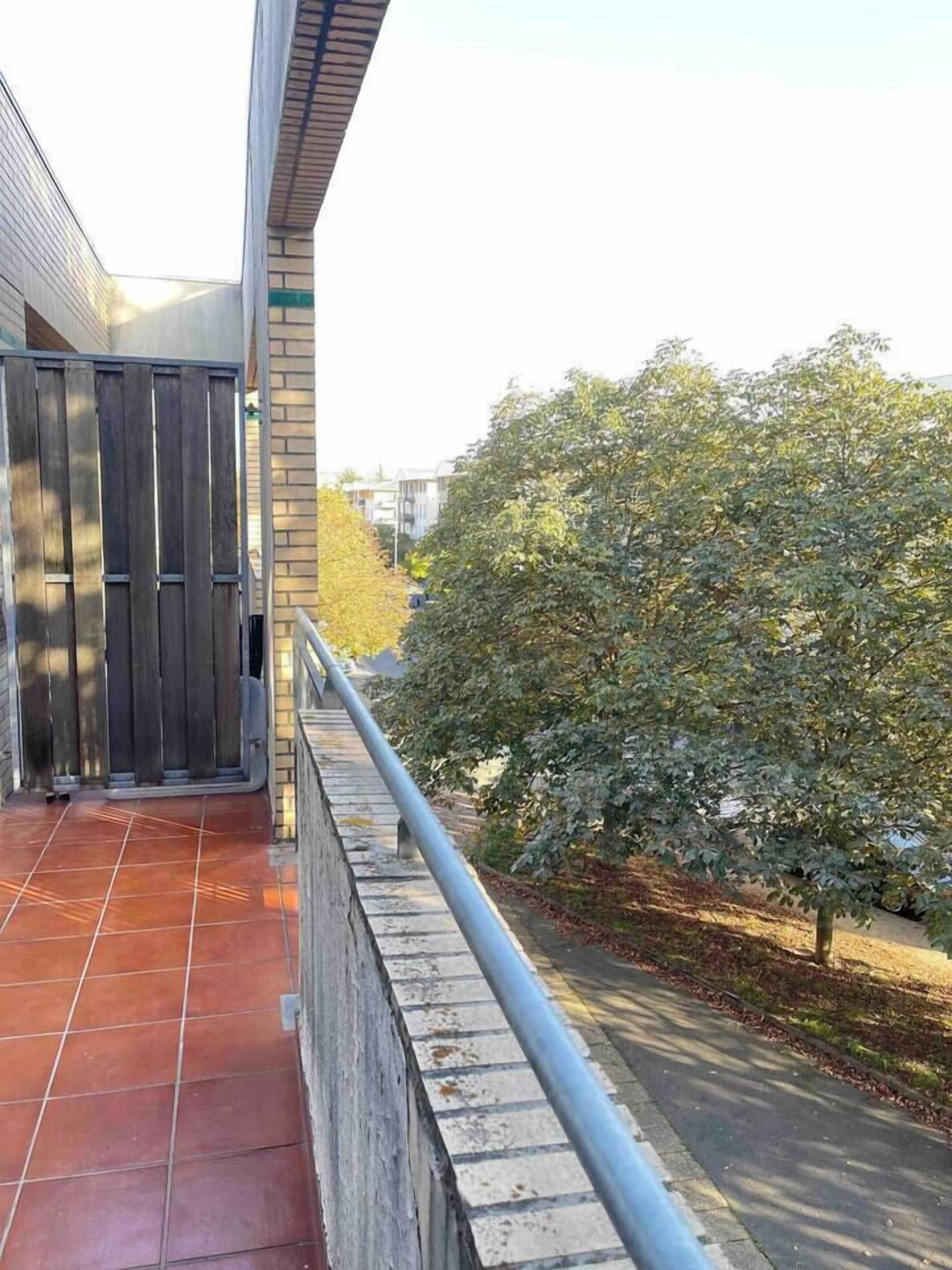 A building entrance with a metal gate, a tiled pathway, and a tree-lined street.