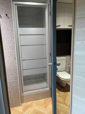 Een moderne badkamer met een glazen douchecabine, een toilet en een kast.