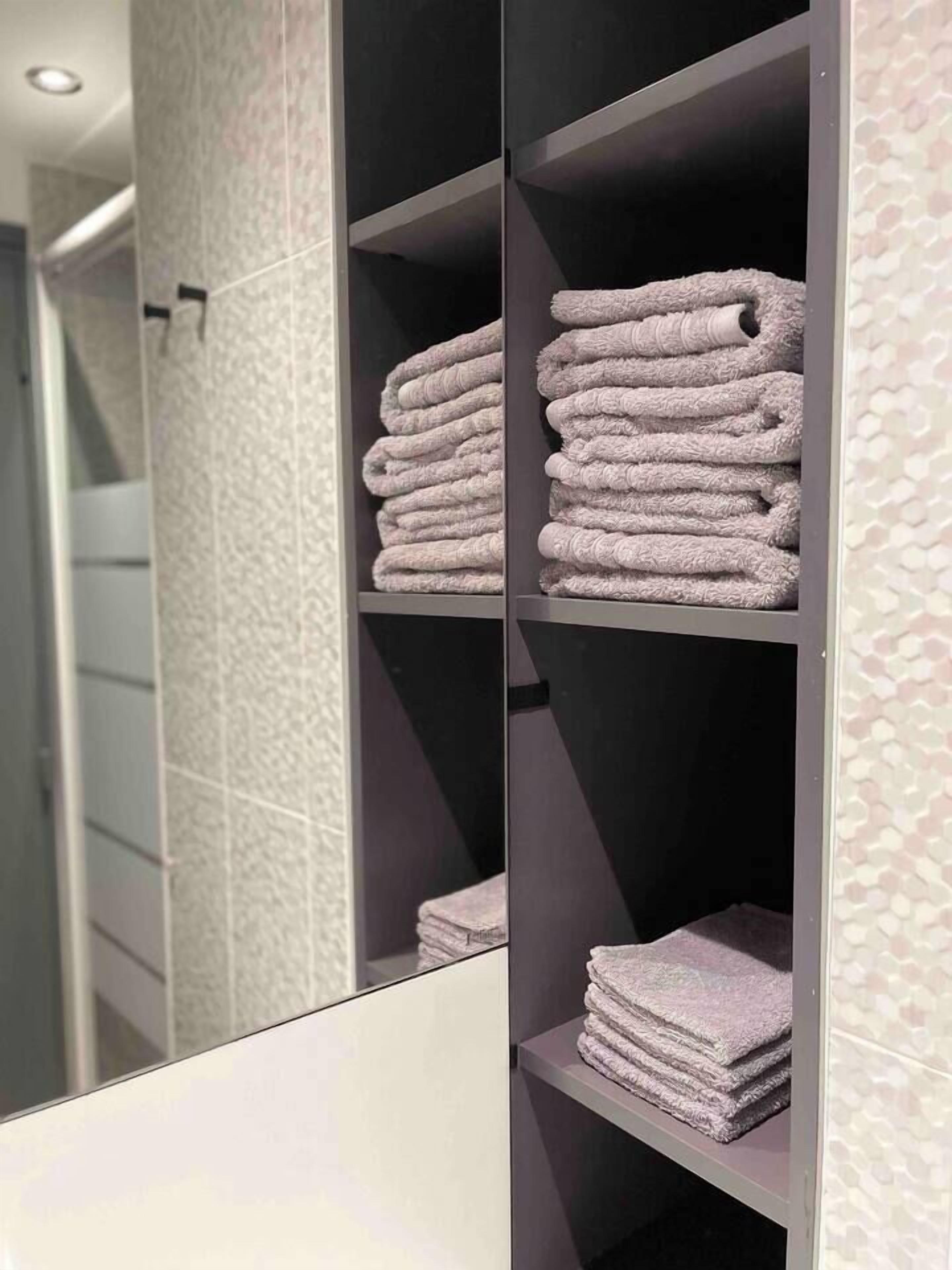 A bathroom with a mirrored vanity, a towel rack with neatly folded towels, and a patterned wall.