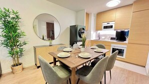 A modern dining area with a wooden table set for four, surrounded by grey upholstered chairs. A large mirror hangs on the wall, and a potted bamboo plant is visible to the left. - T2D Apartment - Suite Gallery Disneyland Paris (Lognes)
