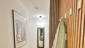 A hallway with wooden paneling, a framed artwork on the wall, a hanging towel, and a mirror. - T2D Apartment - Suite Gallery Disneyland Paris (Lognes)