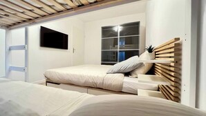 A bedroom with a bunk bed, a window with blinds, a mounted TV, and a wooden headboard. - T2D Apartment - Suite Gallery Disneyland Paris (Lognes)