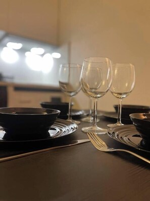 Una mesa de comedor dispuesta con tres copas de vino, un cuenco negro y cubiertos.