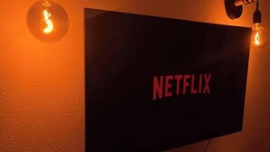 A wall-mounted television with the Netflix logo, surrounded by two wall sconces with light bulbs. - T2D Apartment - Suite UR near Disneyland Paris (Bussy-Saint-Georges)