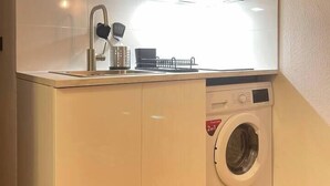A compact kitchen with a built-in washing machine, a sink, and a microwave. - T2D Apartment - Suite UR near Disneyland Paris (Bussy-Saint-Georges)