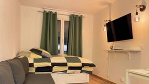 A bedroom with a bed, a sofa, a TV, and a window with curtains.