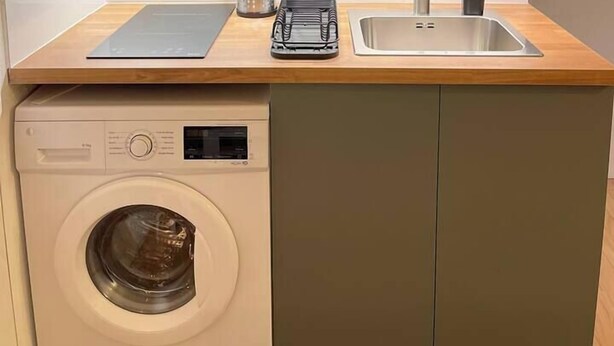 A compact kitchen with a washing machine, a sink, and a countertop with utensils.