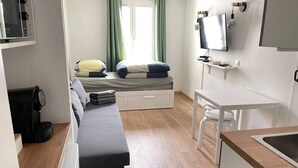 A compact room with a bed, a small table, a kitchenette, and a TV.