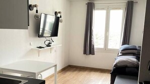 A compact room with a kitchenette, a bed, a TV mounted on the wall, and a window with curtains. - T2D Apartment - Suite BLG near Disneyland Paris (Bussy-Saint-Georges)