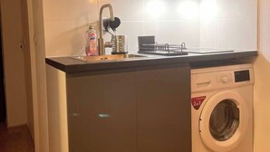 A compact kitchen with a built-in washing machine, a sink, and a small countertop. - T2D Apartment - Suite BLG near Disneyland Paris (Bussy-Saint-Georges)