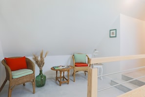 A room with wicker chairs, a small table, a vase with dried plants, and a staircase.