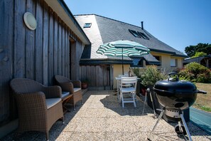 Une terrasse dotée de meubles en osier, d’un barbecue et d’un parasol à rayures.